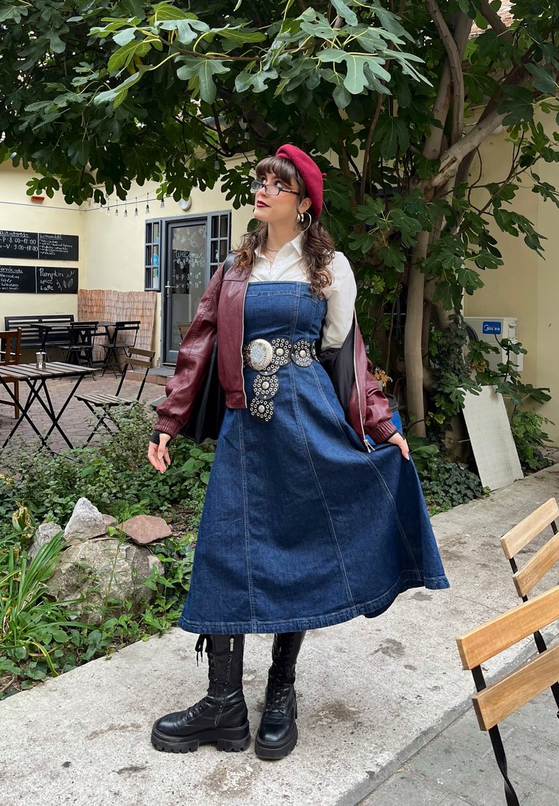 Vestido de mezclilla con un corsé ajustado y falda acampanada, combinado con una chaqueta bomber burdeos. Botas de combate negras y una boina roja completan el look.