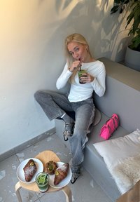 Dva rogljička na belih krožnikih s sladkorjem v prahu, zelena pijača v kozarcu, roza torbica ter oseba v beli majici z dolgimi rokavi.