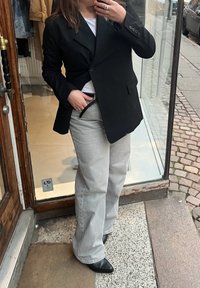 Črn dvojno zapenjajoč blazer, sivi široki hlače in črne gležnjarje. Bel majica pod njim. Očitni dodatki vključujejo prstane.