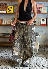 Pantalones cargo en patrón de camuflaje, confeccionados con tejido duradero. Presenta piernas anchas, múltiples bolsillos y un acento de logo. Combinado con una blusa negra ajustada.