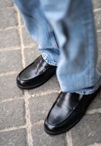 Fekete bőr lakkcipők sima felülettel, részletes varrással és széles pánttal a tetején. Világoskék farmernadrággal viselve.