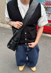 Czarna dzianinowa kamizelka, biała koszulka i luźne niebieskie dżinsy. Czarna skórzana torba na ramię z marszczoną kieszenią. Beżowe buty.