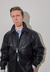 Veste en cuir noir avec un col montant, fermeture éclair et deux poches avant. Texture lisse avec poignets et ourlet côtelés.