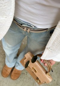Bolso de cuero beige con herrajes dorados, gafas de sol negras, jeans de lavado claro, zapatos de gamuza color arena y un cárdigan de punto texturizado en color crema.