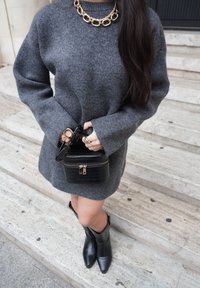 Szürke kötött pulóver leejtett vállal, fekete krokodilbőr mintájú táska és fekete bokacsizma. Kiegészítők: aranylánc nyaklánc és napszemüveg.