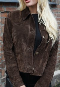 Casaco curto em camurça castanha com gola estruturada, fechos de botão e detalhes de costura visíveis, combinado com um top preto.