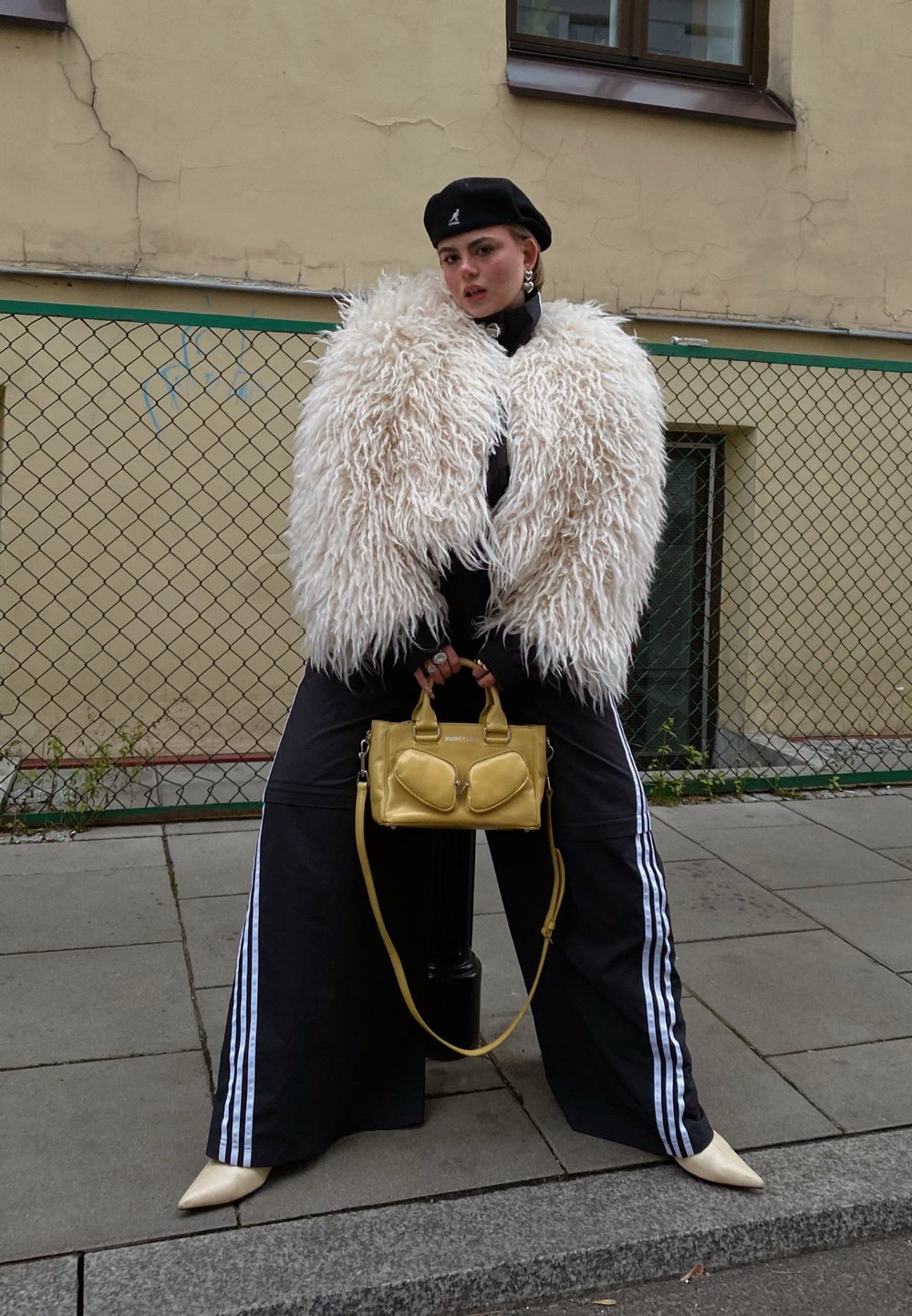 Fluffy white faux fur jacket, black tracksuit trousers with white stripes, yellow handbag, and cream pointy-toed heels. Black beret and accessories.