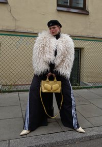 Fluffy white faux fur jacket, black tracksuit trousers with white stripes, yellow handbag, and cream pointy-toed heels. Black beret and accessories.