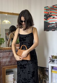 Mustast sametist kleit lillemustriga, mida täiendab pruun nahast käekott struktureeritud disaini ja lühikese sangaga.