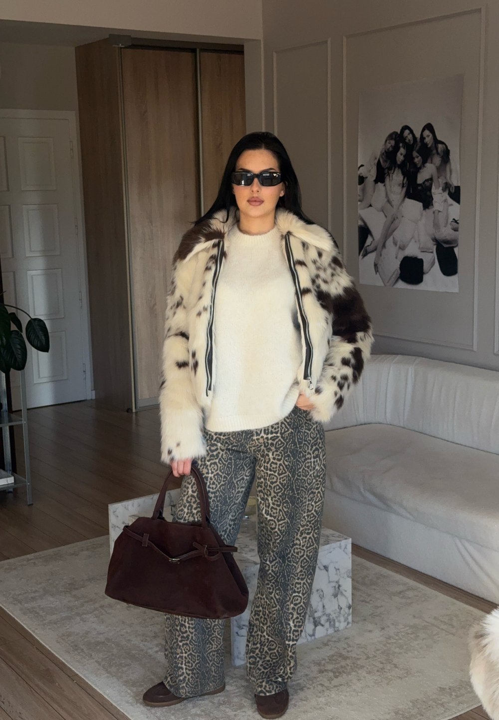 Giacca in pelliccia sintetica con motivi marroni e crema, maglione avorio, pantaloni larghi con stampa leopardata e borsa marrone con design strutturato.