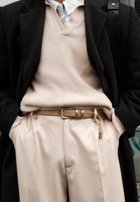 Μπεζ ριγέ πουλόβερ, μαύρο παλτό, κρεμ παντελόνι με πιέτες, ανοιχτό καφέ ζώνη με ασημένια πόρπη και ανοιχτό μπλε ριγέ γραβάτα ορατά.