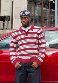 Striped knitted jumper in red and white, featuring a collared neck and ribbed cuffs. Dark jeans and a navy cap with "Yankees" logo. Red car in the background.