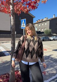 Sveter so vzorom javorových lístkov v hnedej a čiernej farbe, voľného strihu, v kombinácii s bielou košeľou, čiernymi nohavicami a hnedou taškou. Na pozadí jesenné lístie.