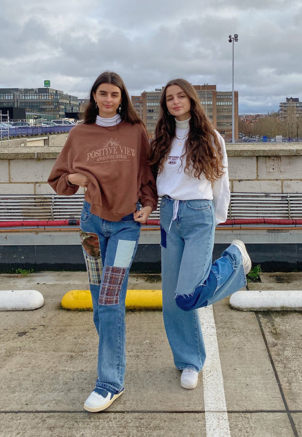 To personer står side om side. Den ene har en brun sweatshirt på med tekst og lapper og slidte jeans; den anden har en hvid bluse og blå jeans.