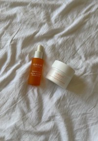 Flacone contagocce di Lumene Nordic-C Glow Boost Essence e barattolo di Glow Moisturizer su uno sfondo di tessuto bianco sgualcito.