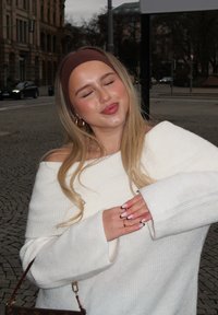 Das Model trägt einen übergroßen, gerippten weißen Pullover mit einem Schulterdesign. Die Haare sind locker und die Nägel haben einen hellrosa Lack mit Akzentdetails.