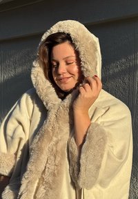 Beige omslag met bontafwerking, voorzien van een capuchon en wijde mouwen. Zachte textuur en een gezellig ontwerp, geschikt voor warme lagen.