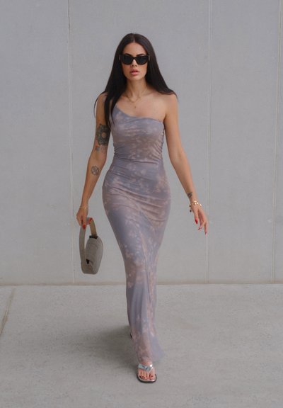 Vestido gris asimétrico con un patrón de tie-dye desvanecido; ajuste elegante, tejido suave, combinado con un bolso gris y sandalias plateadas.