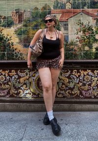 Débardeur noir, shorts imprimé léopard et chaussures noires épaisses avec des chaussettes blanches. Les accessoires comprennent un collier en forme de cœur en argent et un sac à main.