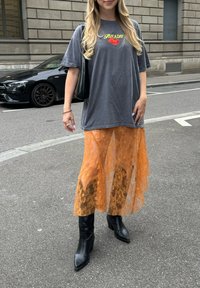 Szürke, oversized póló "Eat a Day" nyomattal, narancssárga csipkés midi szoknya fölött. Fekete, hegyes orrú bokacsizma magas blokk sarokkal.