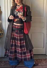 Καφέ δερμάτινο παλτό πάνω από φλοράλ τοπ από δίχτυ, πλισέ φούστα σε κόκκινες και ναυτικές αποχρώσεις, μαύρη ζώνη, κόκκινη τσάντα, στρωματοποιημένο τζιν, πολλαπλά δαχτυλίδια και σκουλαρίκια.