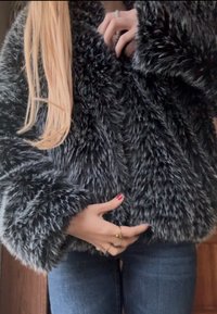 Ξανθό άτομο με κόκκινο βερνίκι νυχιών, φοράει ένα αφράτο ασπρόμαυρο γούνινο παλτό και μπλε τζιν, ρυθμίζοντας το παλτό με τα δύο χέρια.