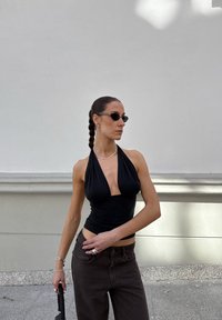 Top negro de halter con escote profundo y diseño ajustado. Combinado con vaqueros de tiro alto marrones. Los accesorios incluyen gafas de sol y collares en capas.