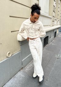 Veste blanche raccourcie avec des détails en lacets, associée à un pantalon blanc ample et des bottines à plateforme. Tissu lisse et texturé.