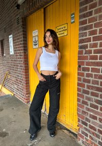 Top court blanc à encolure carrée avec un pantalon cargo noir doté de poches latérales. Debout devant une porte en bois jaune.