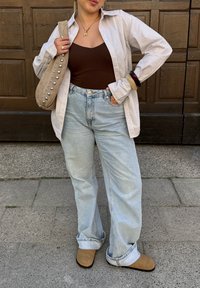 Gestreiftes Hemd, brauner Body, hellblaue weite Jeans, beige Slipper und eine beige Tasche, dekoriert mit silbernen Nieten.