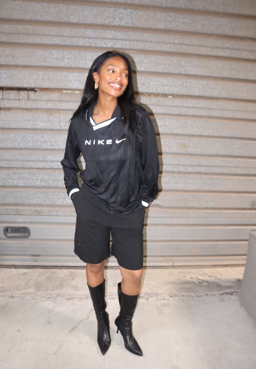 Top de manga longa preto da Nike com colarinho e logótipo brancos, combinado com calções pretos e botas pretas de salto elevado até ao joelho. Texturas suaves no geral.