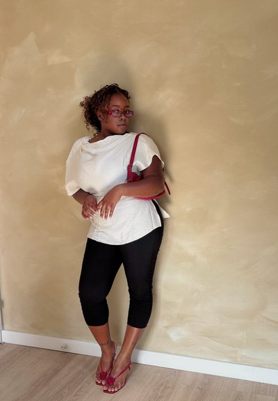 Blusa blanca texturizada con mangas cortas, leggings negros cortos y sandalias rojas con estampado floral. Bolso rojo colgado del hombro. Fondo simple.