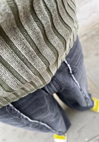 Grey ribbed sweater with green stripes, paired with loose grey jeans featuring distressed details and yellow-accented shoes.