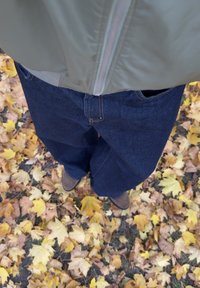 Sinised laia säärega teksad, rohelise jopetega. Maapind kaetud kollaste sügislehtedega. Näha on pruunid jalanõud.