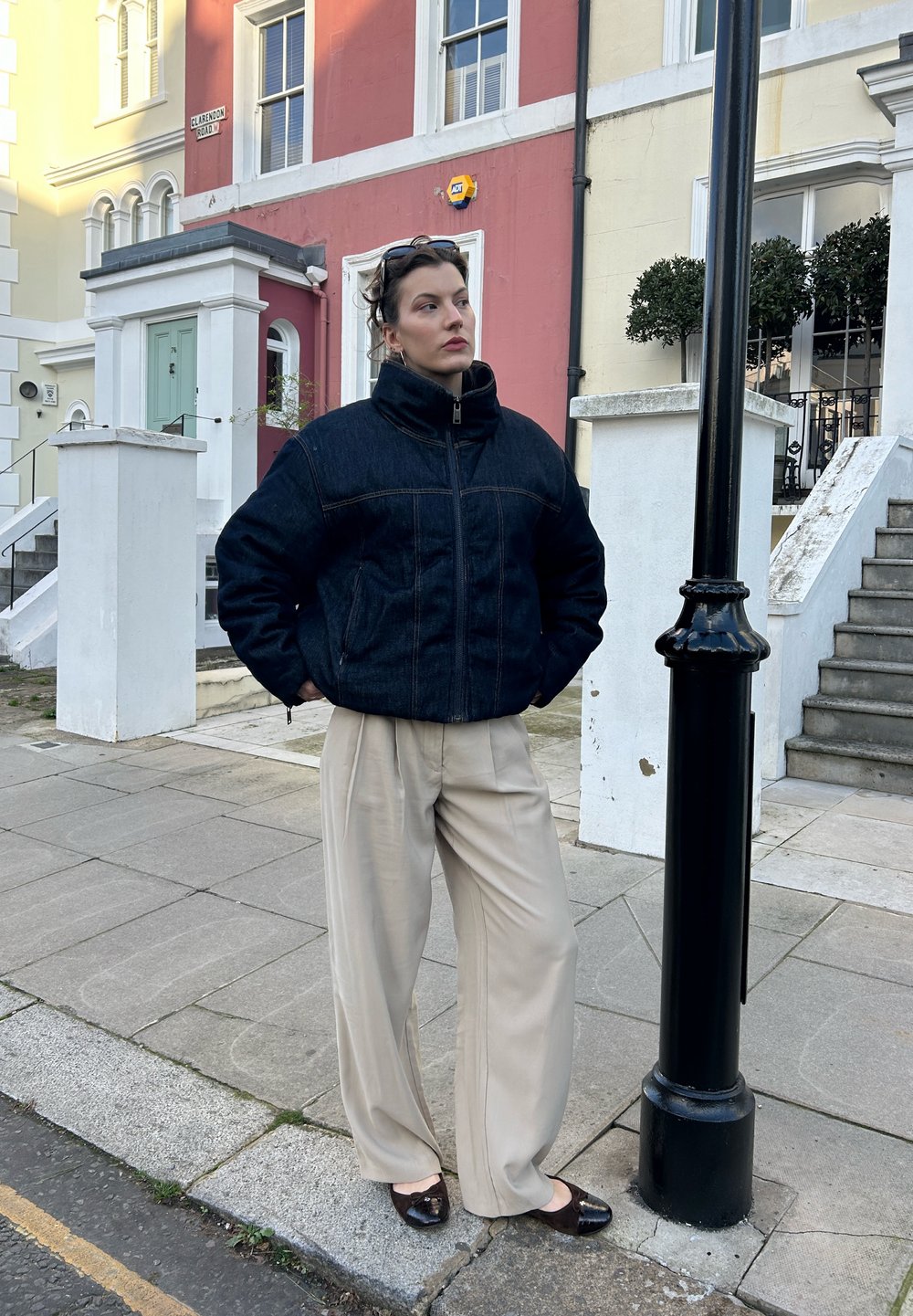 Veste en denim avec col haut et poches frontales, associée à un pantalon beige à jambes larges. Des chaussures plates marron complètent la tenue.