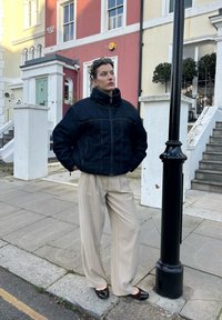 Veste en denim avec col haut et poches frontales, associée à un pantalon beige à jambes larges. Des chaussures plates marron complètent la tenue.