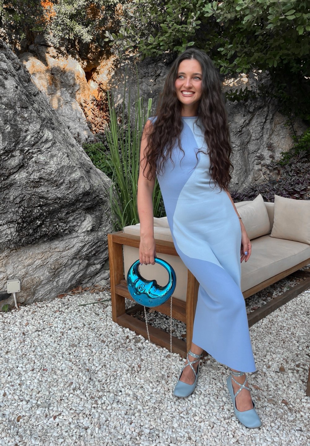 Lichtblauwe, mouwloze jurk met een geometrisch kleurblokontwerp. Accessoire omvat een teal handtas met een ronde handgreep. Vierkante hakken.