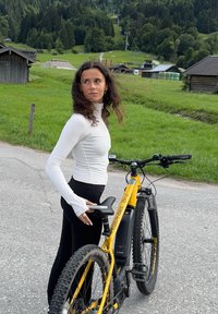 Vélo de montagne électrique noir avec un cadre jaune, pneus épais et un écran numérique. Le cycliste porte un haut ajusté à manches longues blanc et un pantalon noir.