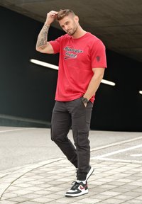 Camiseta roja de manga corta con el texto "Manchester United", combinada con pantalones cargo negros y zapatillas de deporte en blanco y negro con acentos rojos.