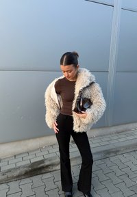 Bež jakna iz umetnega krzna čez rjav oprijet top, združena z visokim pasom črnimi razširjenimi hlačami in temno torbico. Gladke teksture in nevtralni toni.