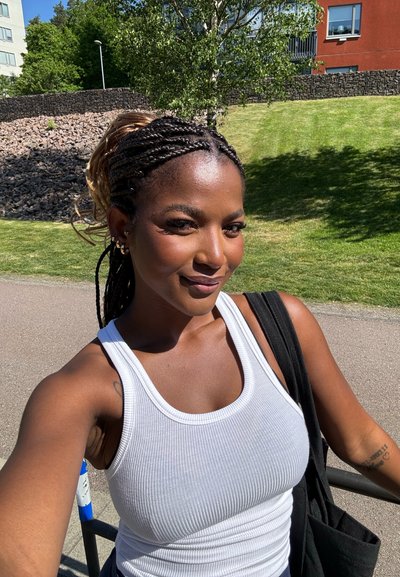 Top sin mangas blanco de canalé con tirantes anchos, combinado con un bolso negro. El tono de piel combina con el entorno al aire libre, con hierba verde y árboles.