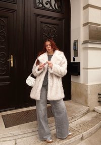 Puhasti bijeli kaput od umjetnog krzna, sivi pleteni pulover, široke sive traperice i srebrne tenisice. Dodatak: mala bijela torbica preko ramena.