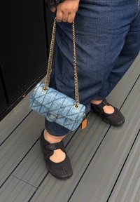 Borsa a tracolla in denim con motivo trapuntato, tracolla in catena dorata e chiusura circolare. Calzature nere con cinturino e design con punta aperta.