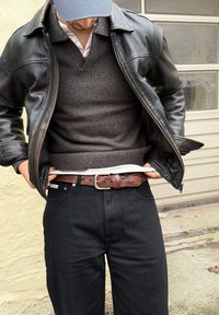 Veste en cuir noire, pull gris, chemise blanche, jean noir, ceinture en cuir marron avec boucle argentée, vue de la taille vers le haut.