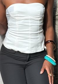 White strapless top with textured fabric, fitted design, and vertical seams. Worn with black pants and multiple bangles in varying colors.