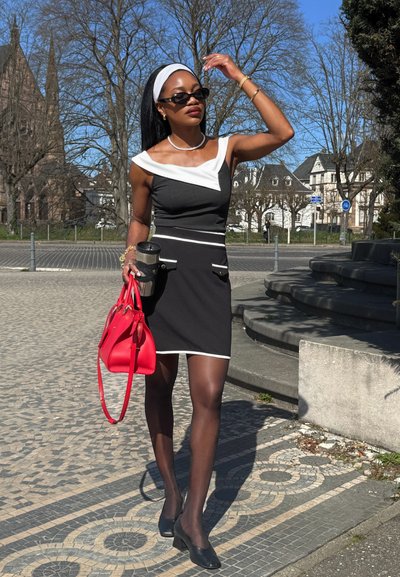 Vestido ajustado en blanco y negro con diseño de hombros al descubierto, que cuenta con dos bolsillos frontales y borde blanco. Los complementos incluyen un bolso rojo y gafas de sol.