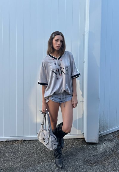 Jersey oversized plateado de Nike con acentos negros y logo, combinado con pantalones cortos grises con volantes y botas negras hasta la rodilla. Bolso gris con la letra K.