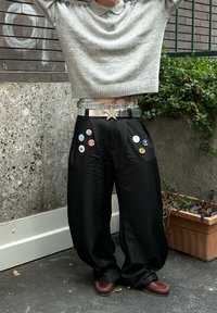 Černé oversized kalhoty s bočními kapsami, zdobené několika knoflíky; spárovány se šedým zkráceným svetrem. Viditelná stříbrná spona pásku ve tvaru hvězdy.