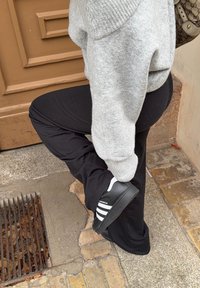 Pantaloni sportivi neri e un maglione grigio abbinati a scarpe Adidas Superstar nere e bianche su un marciapiede con texture.