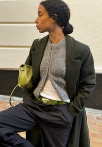 Green wool coat over a grey knit sweater, paired with black trousers. A braided green belt and a small green crocodile-patterned bag.